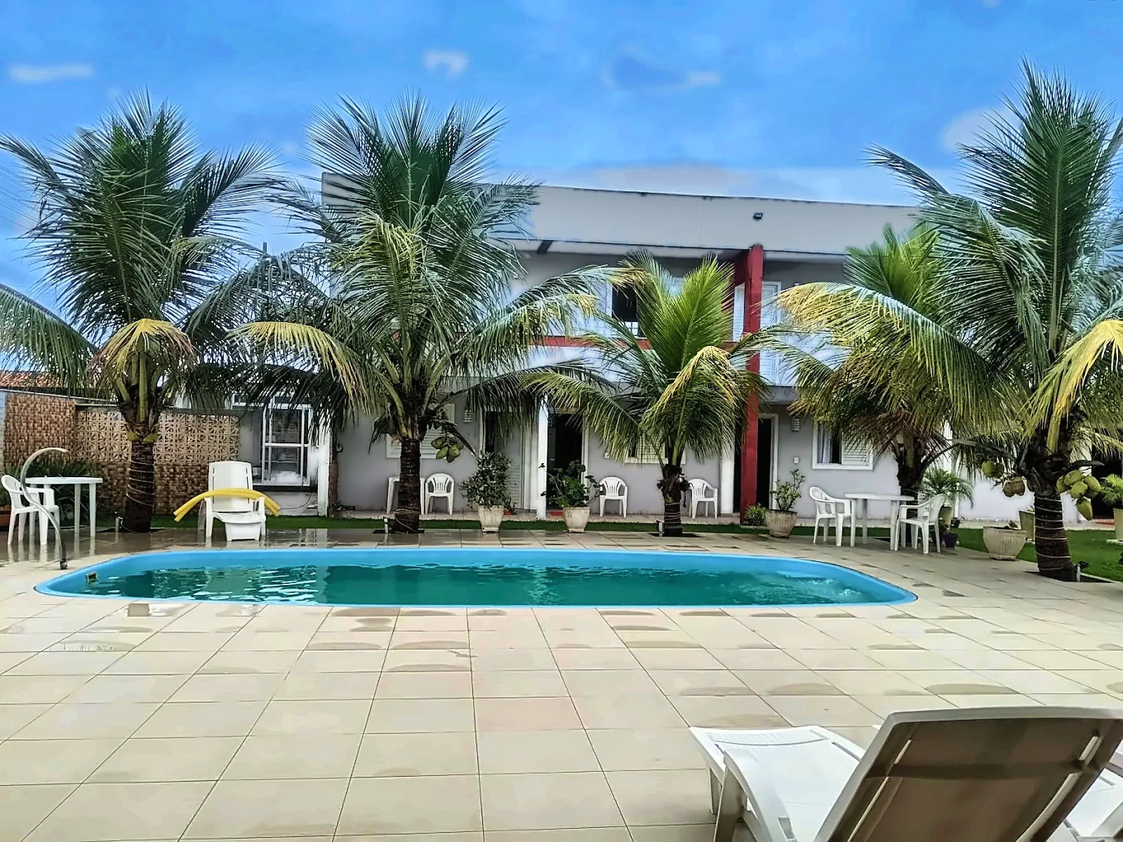 Piscina cercada de coqueiros em frente ao prédio da pousada