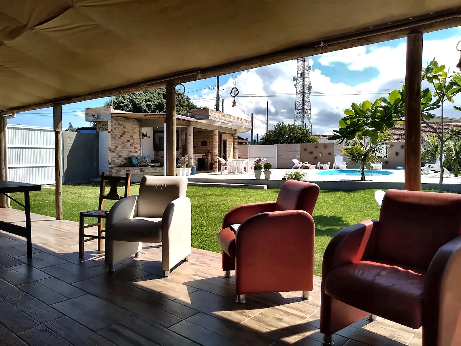 Varanda coberta com poltronas, de frente para o jardim e a piscina