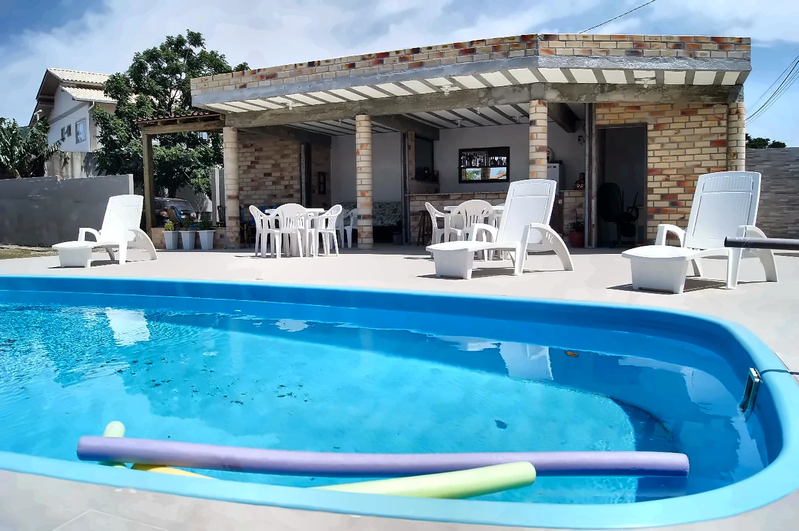 Piscina com espreguiçadeiras e o quiosque de tijolos ao fundo