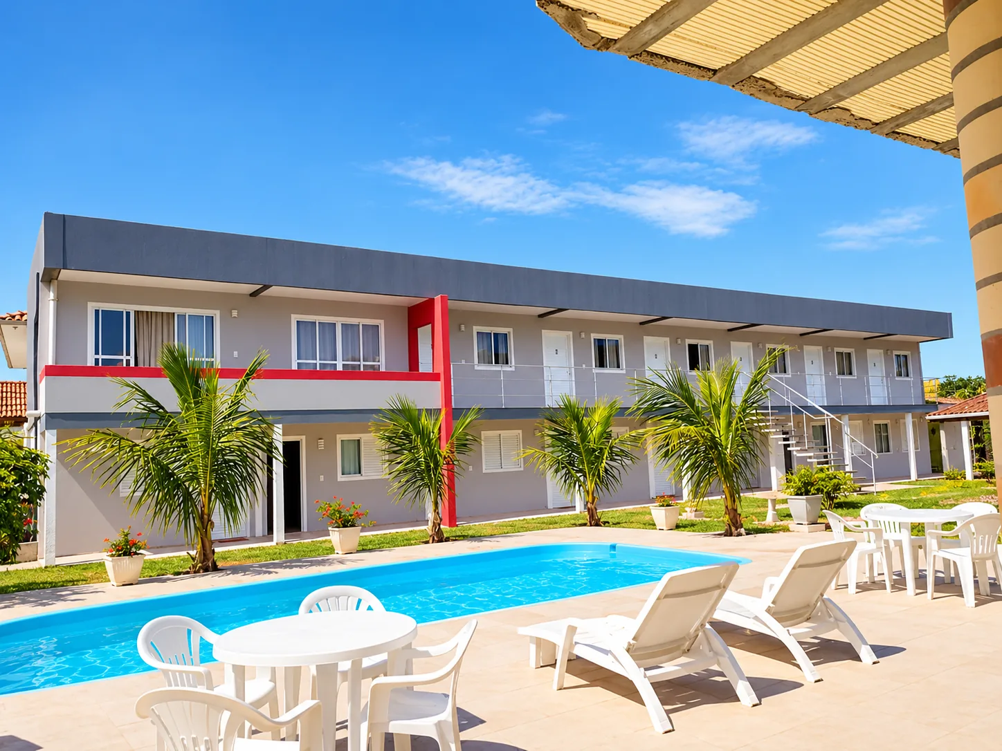 Piscina, espreguiçadeiras e prédio da Pousada Marluah com coqueiros e céu azul na Praia da Pinheira